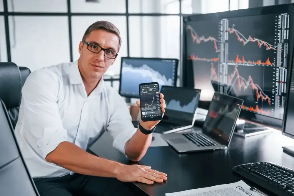 A man is sitting at a desk holding a cell phone.