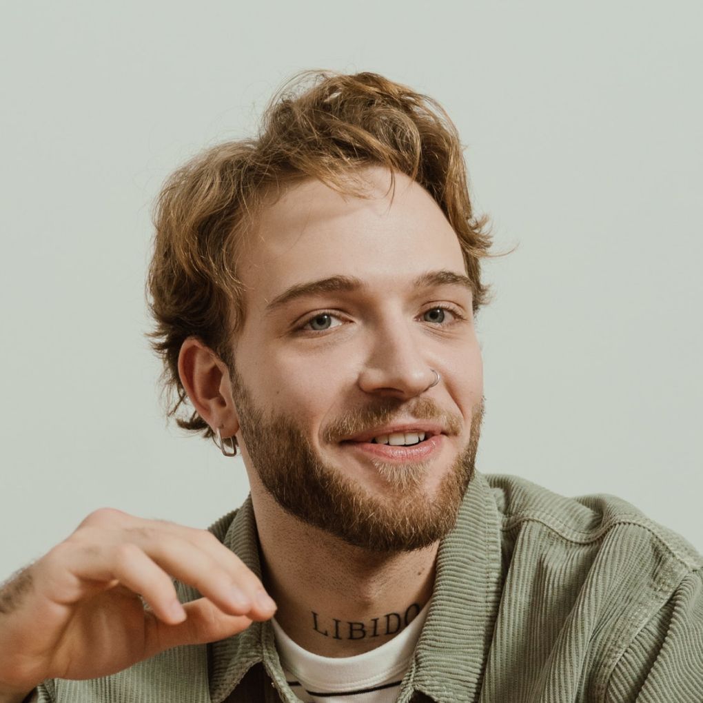 A man with a beard and a tattoo on his neck is smiling.